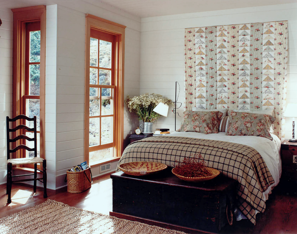 A bright country bedroom with a quilt acting as a headboard.