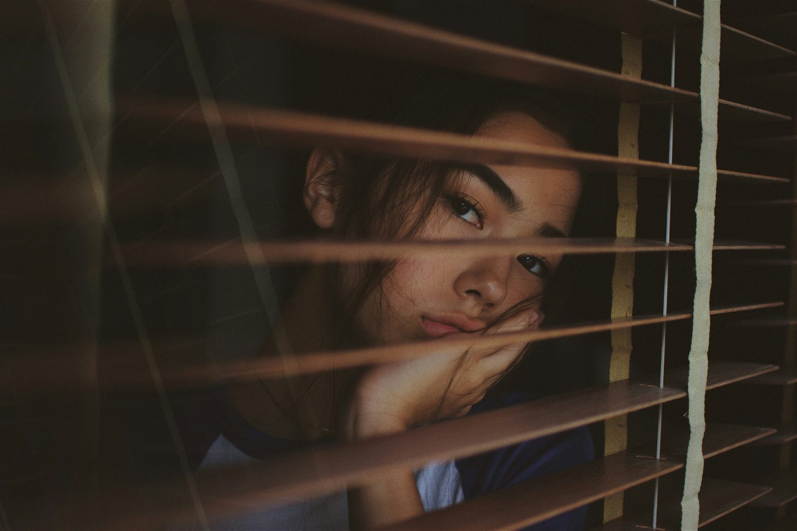 A woman looking through wooden window blinds